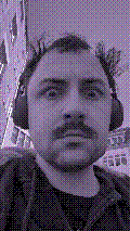 a selfie of a white person, wearing either headphones or a helmet, making an odd expression. the photo is edited to be colorized into a monochrome purple-ish color palette.